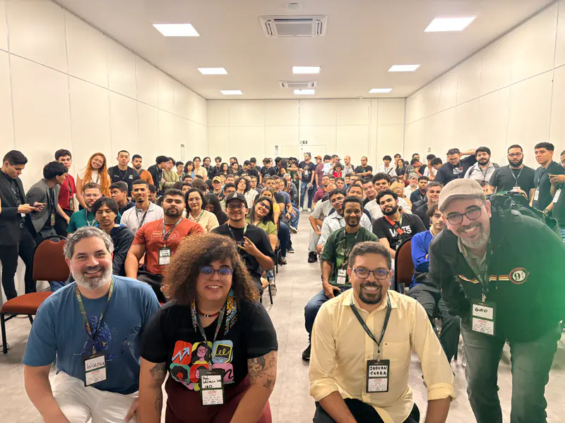 Participantes posam agachados à frente da plateia no auditório.